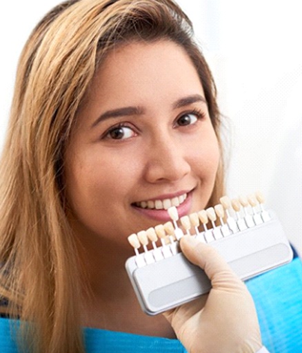 cosmetic dentist in Glenpool holding a row of veneers to a patient’s smile